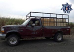 Camioneta tipo pick-up, marca Ford F150, color vino con bidones vacíos.